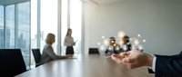 Business professional holding glowing network connections in modern office meeting room with colleagues discussing in background.