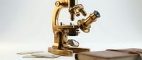 Vintage brass microscope with aged patina displayed on wooden surface with scientific papers, suitable for education, research, laboratory, and historical science concepts.