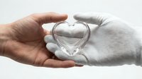 Two hands gently holding transparent glass heart symbolizing love, care, compassion and emotional connection on white background isolated for design.