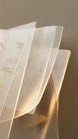 Stack of translucent architectural blueprints with technical drawings and topographic lines, backlit with warm golden light against neutral background for design projects.