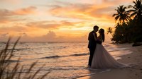 Romantic couple silhouette embracing on tropical beach at golden sunset with palm trees and ocean waves for wedding photography and love concepts.