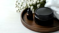 Minimalist spa composition with black cosmetic jar, essential oil dropper bottle on wooden tray with white flowers and towel against light background.