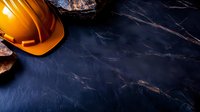Orange construction hard hat on dark marble or stone surface with dramatic lighting, creating contrast between safety equipment and luxurious texture background.