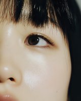 Close-up macro shot of Asian female eye with natural makeup, black straight bangs, and flawless glowing skin showing skincare and beauty concept.