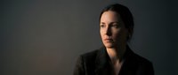 Professional businesswoman in dark suit with confident expression against moody lighting background for corporate and leadership concepts.