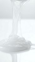 Transparent viscous liquid pouring and stretching, creating elastic strands and pooling on white surface for cosmetic, skincare, or industrial product applications.