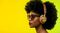 Young African American woman with afro hairstyle wearing sunglasses and gold headphones against bright yellow background for music and lifestyle content.