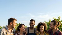 Young diverse group of friends smiling together outdoors in vineyard setting during daytime, suitable for lifestyle, friendship, community and social media content.
