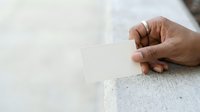 Close-up of a hand holding a blank white card against a concrete surface, suitable for mockups, branding, and business presentations.