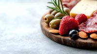 Gourmet charcuterie board with cured meats, aged cheese, fresh strawberries, olives, nuts and herbs on wooden platter for entertaining and appetizers.