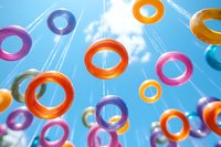 Colorful floating rings against bright blue sky background create dynamic composition with orange, pink and purple elements casting soft shadows.