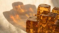 Amber glass ice cubes casting warm shadows on a light surface, suitable for beverage photography, luxury drink advertising, and cocktail styling projects.