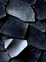 Dark geometric fragments of broken glass create abstract pattern with metallic sheen and sharp edges, dramatic lighting highlights textural details and shadows.