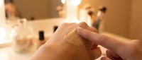 Woman applying moisturizing cream to her hand in a bright bathroom setting, skincare routine and cosmetic product usage for beauty and wellness purposes.