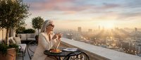 Elegant blonde woman enjoying morning coffee on luxury rooftop terrace overlooking city skyline at sunrise with warm golden light and urban landscape view.