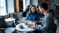 Young couple enjoying coffee date conversation at cozy cafe with vintage interior design and natural lighting creating warm romantic atmosphere.