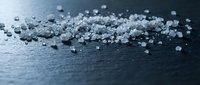 Close-up of sea salt crystals scattered on dark wet surface with water droplets, suitable for culinary, food styling, and health and wellness content.