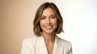 Professional young Caucasian businesswoman with short brown hair smiling confidently in beige blazer against neutral background for corporate marketing.