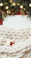 Festive holiday flat lay with evergreen garland, warm string lights, red accents, chunky knit blanket, and decorative sheep ornament on white background for seasonal marketing and greeting card designs.