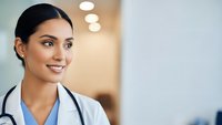 Young female doctor with stethoscope smiling confidently in modern medical facility, healthcare professional ready for patient care and consultation.