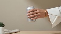 Professional woman hand holding white coffee cup with gold bracelet in modern minimalist workspace setting for business lifestyle concepts.