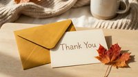 Autumn thank you card with golden envelope and red maple leaf on wooden table, cozy fall season greeting concept.