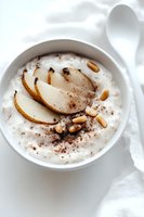 Creamy rice pudding topped with poached pear slices, pine nuts and chocolate powder in white ceramic bowl on light background. Perfect for dessert menu.