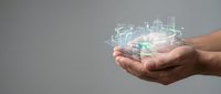 Hand holding glowing digital hologram of architectural building wireframe model against gray background for technology and construction concepts.