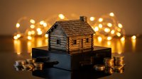 Wooden miniature house model on dark surface with golden bokeh lights and coins representing real estate investment and property savings concept.