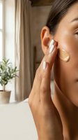 Young woman applying facial serum or oil to skin in bright bathroom interior for skincare routine and wellness lifestyle.