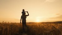 Adult male farmer in silhouette standing in golden wheat field at sunset, shading eyes while observing crops. Agricultural work and harvest.