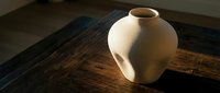 Cream ceramic vase with organic rounded form sits on rustic wooden surface, showcasing minimalist pottery design and natural lighting for home decor.