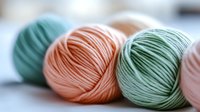 Colorful yarn balls in pastel mint, peach, and sage green tones arranged together, showcasing soft textile textures for knitting and crochet projects.