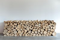 Neatly stacked firewood logs arranged in modern minimalist style against white wall, showing natural wood texture and organic shapes for interior design.