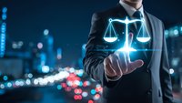 Professional businessman in dark suit touching glowing digital justice scales hologram against blurred city lights background at night.