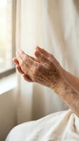 Elderly hands cupped in prayer or meditation gesture by window with soft natural light creating peaceful spiritual moment for wellness and faith concepts.