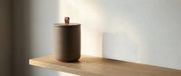 Minimalist ceramic canister with wooden lid on natural wood shelf against white wall in modern kitchen interior design for storage and organization.
