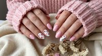 Young woman hands in cozy pink knitted sweater showing trendy nail art manicure with floral design and pastel polish for beauty salon services.