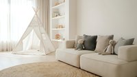 Modern minimalist children's playroom with white teepee tent, beige sofa, built-in shelving, and natural jute rug creating cozy Scandinavian nursery interior.