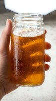 Close-up of a hand holding a glass jar filled with cold cola or iced tea beverage with condensation droplets, perfect for beverage advertising and refreshment concepts.