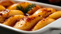 Ripe peach halves with spices and honey in white baking dish, macro food photography showing juicy fruit dessert ready for roasting. Fresh herbs garnish.