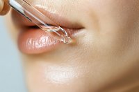 Close-up of woman applying clear lip gloss with glass applicator wand for beauty skincare routine and cosmetic makeup enhancement.