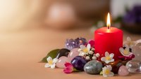 Red candle burning surrounded by healing crystals amethyst rose quartz and white flowers on wooden surface for meditation wellness spa relaxation therapy.