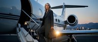 Mature blonde woman in business suit boarding private jet at sunset, representing luxury travel, executive lifestyle, and corporate success for premium business concepts.