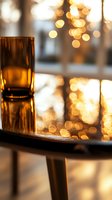 Glass of amber liquid on wooden table with soft golden bokeh lights creating warm atmospheric mood, suitable for beverage advertising and holiday themes.