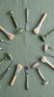 Facial massage tools and makeup brushes arranged in circle on green linen background for skincare and beauty routine flat lay composition.
