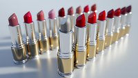 Row of luxury metallic lipsticks in various pink and red shades arranged in diagonal line on reflective surface with soft lighting and shallow depth of field.