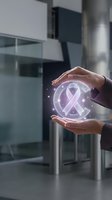 Hands protecting glowing purple awareness ribbon symbol in modern office environment representing cancer support and healthcare advocacy.