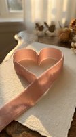 Rose gold satin ribbon shaped into heart on white fabric with warm sunlight and dried flowers creating romantic Valentine's Day atmosphere.