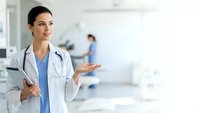 Professional female doctor in white coat with stethoscope presenting in modern hospital setting with medical team background for healthcare marketing.